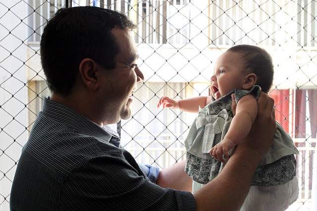 Na foto, um pai levantando sua filha bebê sorrindo
