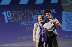 Foto em que cineasta Vladimir Carvalho entregando prêmio a estudante vencedor das categorias melhor roteiro e melhor direção
